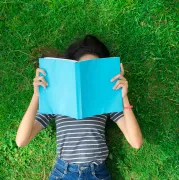 Young woman laying in the grass reading a book.