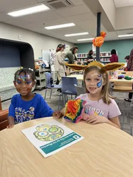 Photo of two children at a table with face paint