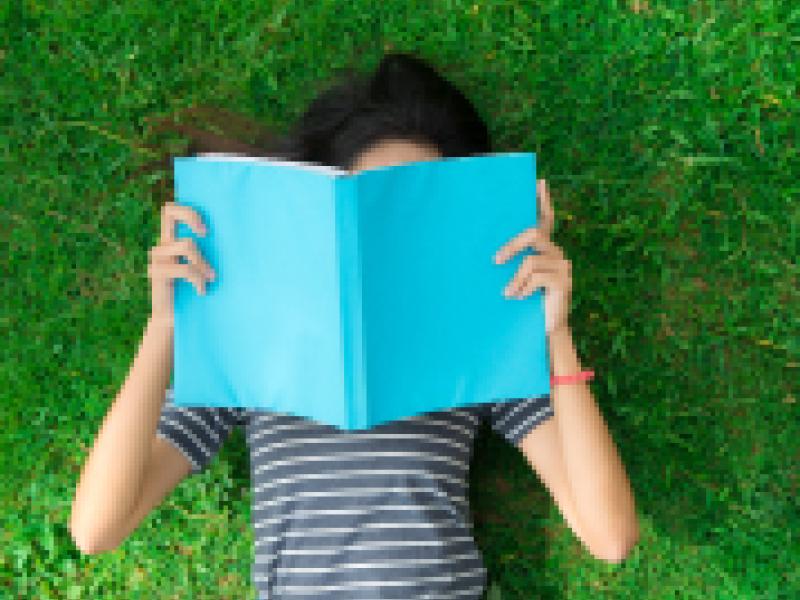 Young woman laying in the grass reading a book.