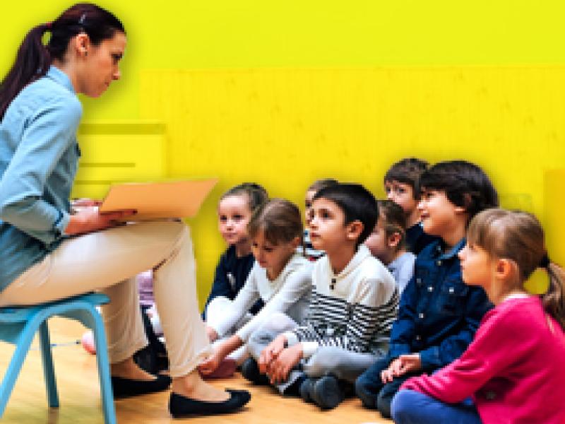 Photo of a woman reading a book to children sitting on the floor