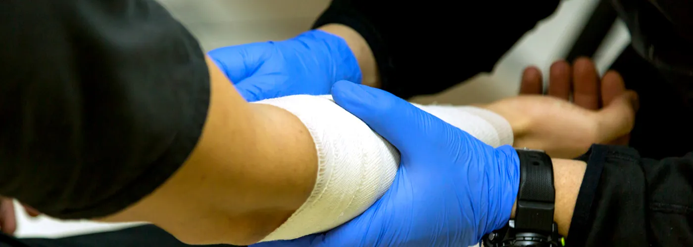 An arm being bandaged with hands in blue medical gloves