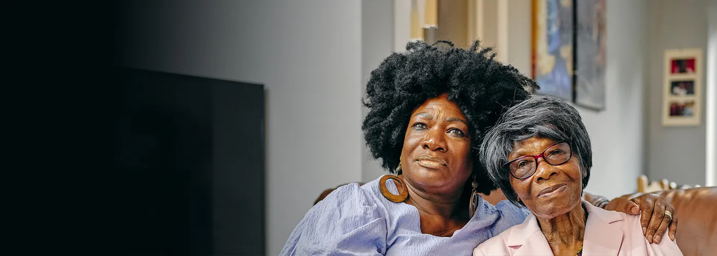 an elderly woman and her caregiver daughter holding each other