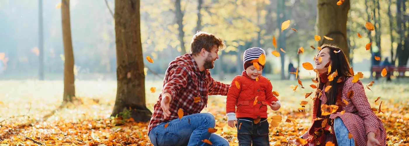 a family of three outside enjoying the fall leaves